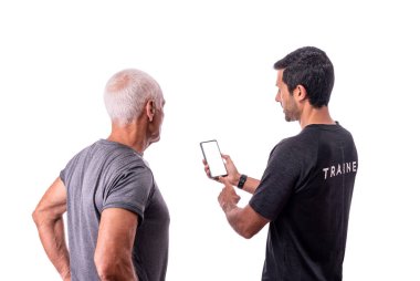 Bir fitness eğitmeni yaşlı bir müşteriye beyaz izole edilmiş bir arka planda nasıl yazılım uygulaması kullanılacağını açıklar..