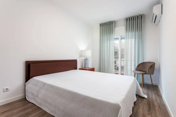 Dormitorio bien iluminado por una lámpara, con cama blanca, una ventana y un bonito conjunto de cortinas para cubrirlo. —  Fotos de Stock