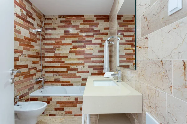 Semplice bagno a tema beige decorato con alcuni asciugamani puliti. C'è un lavabo moderno accanto a una doccia, illuminato da una finestra verso l'esterno. — Foto Stock