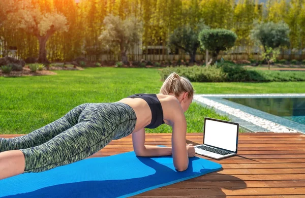 Donna sta praticando ginnastica fitness, pilates, all'aperto vicino casa e piscina, lezioni online con un allenatore. Con uno sfondo al giardino. — Foto Stock