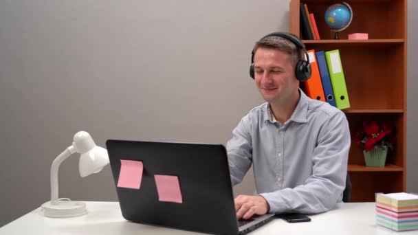 Egy fiatal munkavállaló kommunikál egy ügyféllel egy online konferencián az irodából, fejhallgatón keresztül.. — Stock videók