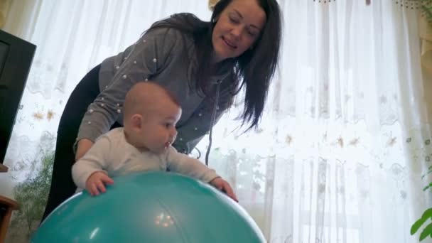 Uma jovem mãe na sala de estar, fazendo ginástica com o bebê, reabilitação, em uma bola de ginástica. — Vídeo de Stock