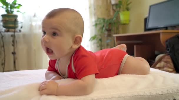 Un bebé sano recién nacido, un niño de cuatro meses, yace boca abajo, descansando felizmente. Sobre el fondo de la habitación. — Vídeos de Stock