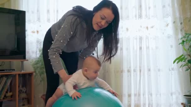 Молодая мама в гостиной, занимается гимнастикой с ребенком, реабилитацией, на гимнастическом балу. — стоковое видео