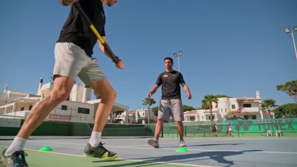 Sportler, der mit Hilfe seines persönlichen Trainers auf einem Tennisplatz sein Tennisvolley mit einem Widerstandsband übt. Faro Portugal 17. April 2021 — Stockvideo