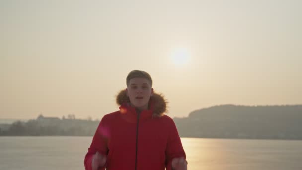 Un ragazzo della razza europea, con una giacca rossa, canta una canzone rap. Sul mare, a metà del tiro. — Video Stock