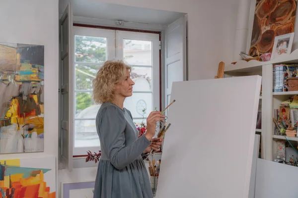 En kvinna konstnär teckningar, förbereder sig för att skapa en kreativ bild, framför henne är en tom duk. Kopiera krydda. I galleriets egen ateljé, studio. — Stockfoto