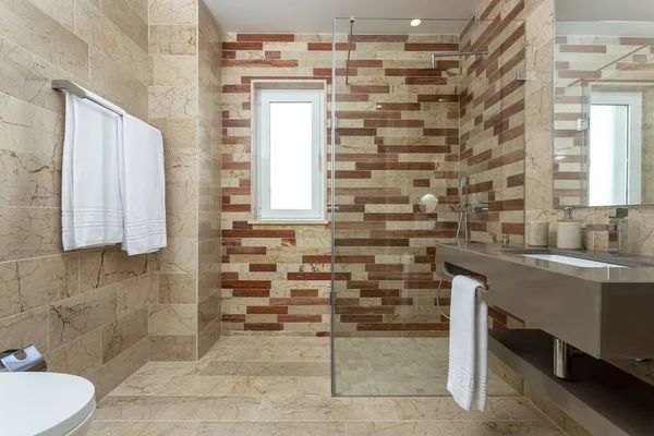 Baño de temática beige simple decorado con algunas toallas limpias. Hay un moderno lavabo junto a una ducha, iluminado por una ventana al exterior. — Foto de Stock