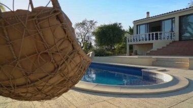 Lüks sallanan sandalye, temiz havuz ve villanın yanında. Güzel bir bahçe ve yaz havasında gökyüzü. Kamerayı ileri al..