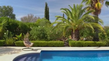 Lüks sallanan sandalye, temiz havuz ve villanın yanında. Güzel bir bahçe ve yaz havasında gökyüzü. Kamerayı ileri al..