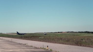 Uzakta bir F-16, bir askeri jet uçağı taksicilik yapıyor, bir havaalanından kalkmaya hazırlanıyor..