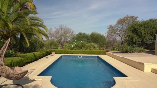 Chaise à bascule suspendue luxueuse, à côté de la piscine propre et de la villa résidence. Avec un beau jardin et ciel par temps d'été. Avancez la caméra.. — Video