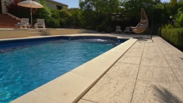 Luxurious hanging rocking chair, next to the clean pool and villa residence. With a beautiful garden and sky in summer weather. Move the camera forward. — Stock Video