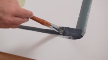 Kadın ressam tuvale fırça darbeleriyle boya uyguluyor, yakın plan fırça çekiyor. Soyut resim.