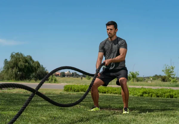 Male athlete on the outdoor in the park, exercises for endurance, using a thick rope, for cross fitness. European Caucasian — Stock Photo, Image