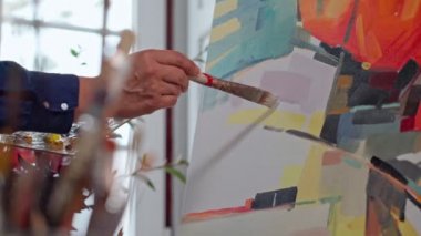 Kadın ressam tuvale fırça darbeleriyle boya uyguluyor, yakın plan fırça çekiyor. Soyut resim.