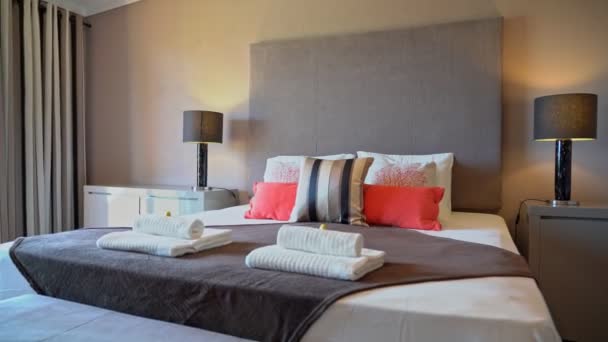 Acogedor dormitorio moderno con una cama en un hotel, hogar para el descanso, el sueño. Toallas dobladas. Mesitas de noche con lámparas de mesa. — Vídeo de stock