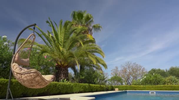 Chaise à bascule suspendue luxueuse, à côté de la piscine propre et de la villa résidence. Avec un beau jardin et ciel par temps d'été. Avancez la caméra.. — Video
