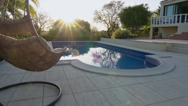 Luxusní houpací křeslo, vedle čistého bazénu a vilové rezidence. S krásnou zahradou a oblohou v letním počasí. Posuňte fotoaparát dopředu. — Stock video