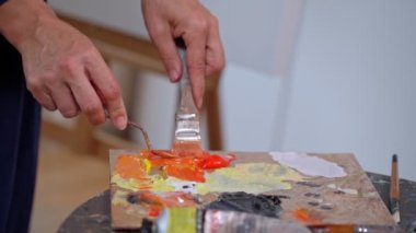 Palette bir kadın sanatçı, yağlı boyaları karıştırarak yeni bir tablo çiziyor. Yakın plan. Yavaş çekim
