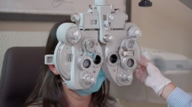 Optik foropteri olan genç bir kadının görme ölçüsü. Göz testi yapan bir kadın. Kız ve maskeli doktor bir salgın içindeler. Kapat.