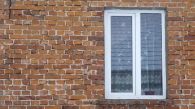 Kış sıkıcı dramatik sahne, arka planda kırmızı tuğla bir duvarın üzerine düşen kar. Yan taraftaki pencere. Yavaş çekim.