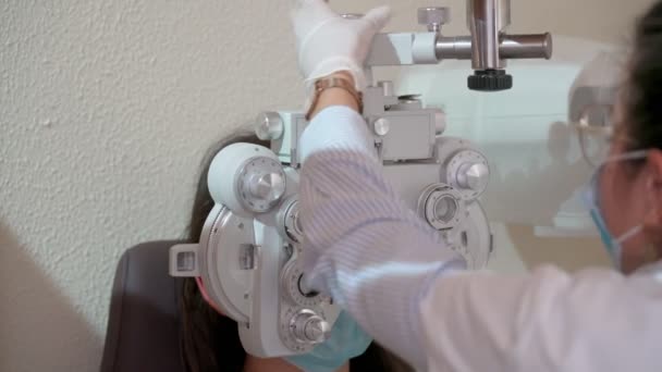 Optik foropteri olan genç bir kadının görme ölçüsü. Göz testi yapan bir kadın. Maskeli bir kız ve doktor salgın halinde. Kapat. — Stok video