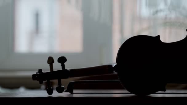 Silhouet van een antieke viool op een houten tafel, een boog en een venster op de achtergrond. Dramatische muzikale stemming. — Stockvideo