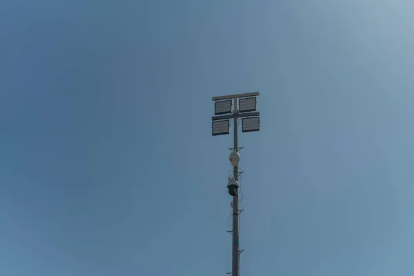 A street pole with surveillance cameras, in a criminal zone, and night lighting lamps. Against the blue sky.