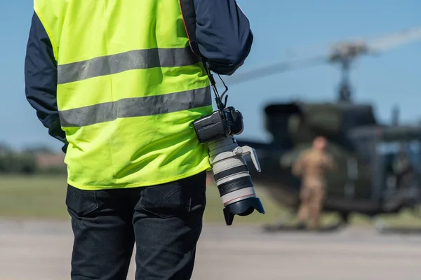 Un photographe militaire, un journaliste, vêtu d'un gilet jaune signal, prêt à travailler devant un hélicoptère militaire. Gros plan. Le fond est flou. Photos De Stock Libres De Droits