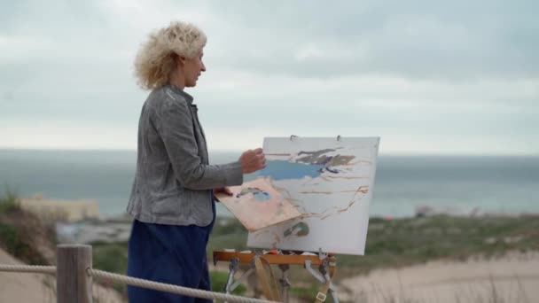 Middelbare Europese vrouw, kunstenaar, schildert een zeegezicht met een origineel uitzicht op de zee. Langzame beweging — Stockvideo