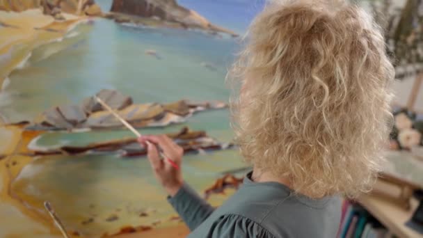 Middle-aged white woman artist paints a picture with paints. Close-up background. — Stockvideo