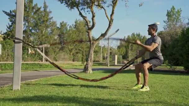 Parkta antrenman yapan orta yaşlı bir sporcu. Vücudu elastik bantlarla çalıştırmak. Mavi gökyüzü. — Stok video