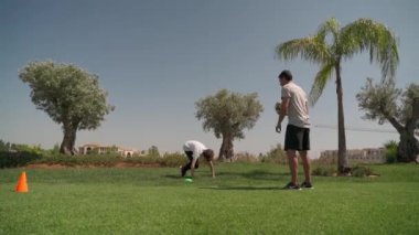 Yeşil sahada antrenman yapan genç bir adam futbol oynuyor. Koordinasyon ve hız için engellerle koşmak.