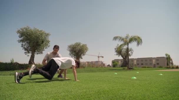 Entraîneur d'âge moyen à l'entraînement dans le parc avec un jeune homme. Exercice push-ups et courir. Journée ensoleillée. — Video
