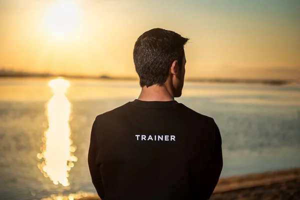 Brunette man stands with his back looking at the seascape of sunrise. Concept, fitness trainer, advertising on back. — Stock Photo, Image