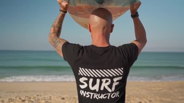 男冲浪者教练带着纹身，头顶着一块木板走向大海。葡萄牙Faro 2021 — 图库视频影像