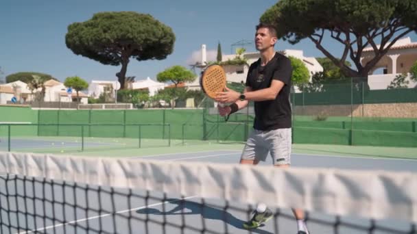 Un atleta si allena colpi su un campo da tennis, attraverso la rete nel padel gioco, Con una racchetta di legno. Faro Portogallo 2021 16 aprile — Video Stock