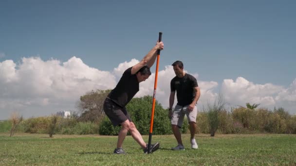 Un entraîneur de fitness avec un client, dans un parc sur une prairie verte, faire des étirements à l'aide d'un bâton de gymnastique, bâton. Portugal Faro 2021 15 mars — Video