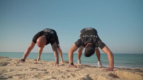 Un surfista simula il sollevamento del corpo su una tavola, sulla spiaggia, con un istruttore per insegnare le abilità di surf. Un principiante in una scuola di surf. Portogallo Faro 2021 15 marzo — Video Stock