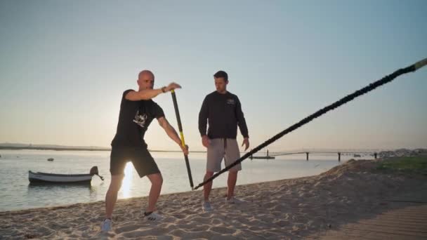 An athlete on the beach, trains simulates rowing on a surfboard and receives instructions from a personal fitness trainer. Preparing for competitions. Portugal Faro 2021 March 15 — Stock Video