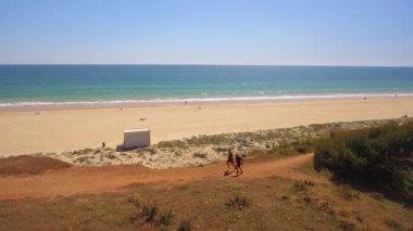Okyanus kıyısında koşan spor hocasıyla yaşlı bir adamın hava manzarası. Yeşilliğe bulanmış bir uçurum. Yan görüş. Güneşli bir gün. 