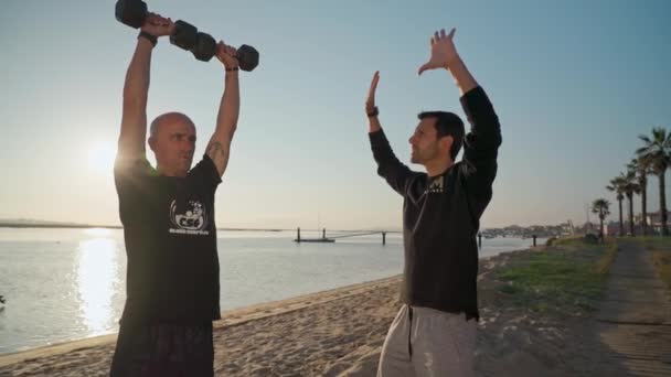 一个在海滩上的运动员，带着哑铃训练，并接受个人健身教练的指导。去参加冲浪比赛葡萄牙Faro 2021 — 图库视频影像