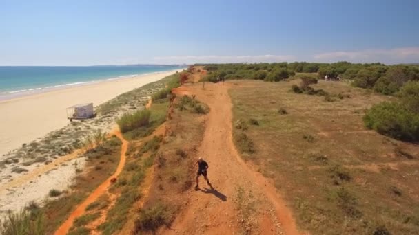 Luftaufnahme eines älteren Mannes, der an der Meeresküste entlang läuft. Eine Klippe im Grünen. Sonniger Tag. Frontansicht. — Stockvideo