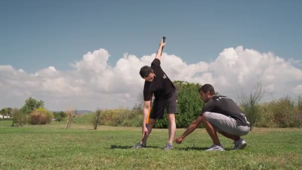 Un entraîneur de fitness avec un client, dans un parc sur une prairie verte, faire des étirements à l'aide d'un bâton de gymnastique, bâton. Portugal Faro 2021 15 mars — Video