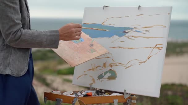 Une artiste d'âge moyen dans la nature peint un tableau. Mélange de peintures sur une palette. Gros plan. — Video