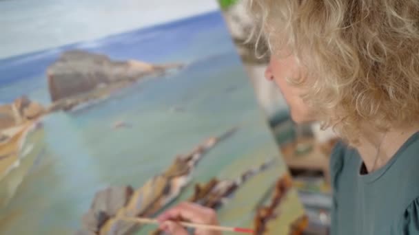 La artista blanca de mediana edad pinta un cuadro con pinturas. Taller de arte. Fondo de primer plano. — Vídeos de Stock