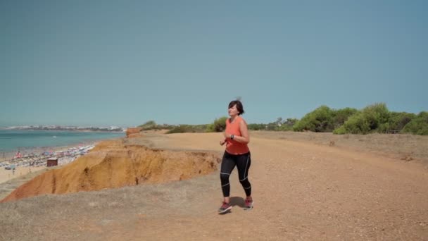 Wanita paruh baya, obesitas, berlari untuk menurunkan berat badan dan angka, dalam gerakan lambat. Di pantai dengan pemandangan dari pantai.. — Stok Video