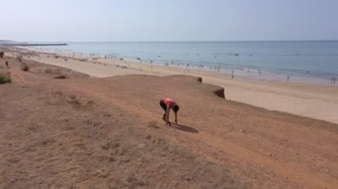Orta yaşlı bir kadın, kilolu, kardiyo koşusu yapıyor, kumsalda, kilo vermek için. Arka planda deniz manzarası.