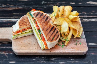 Sebzeli ve otlu ızgara sebzeli sandviç. Tahta mutfak tahtasında ikiye bölünmüş. Patatesli garnitür. Yakın plan..